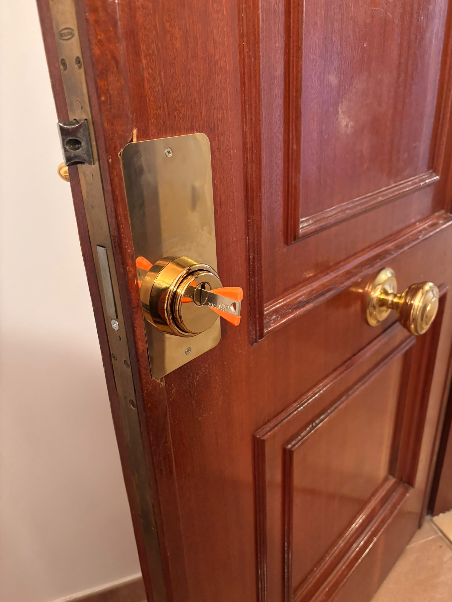 Bombín de seguridad con llave naranja en puerta madera