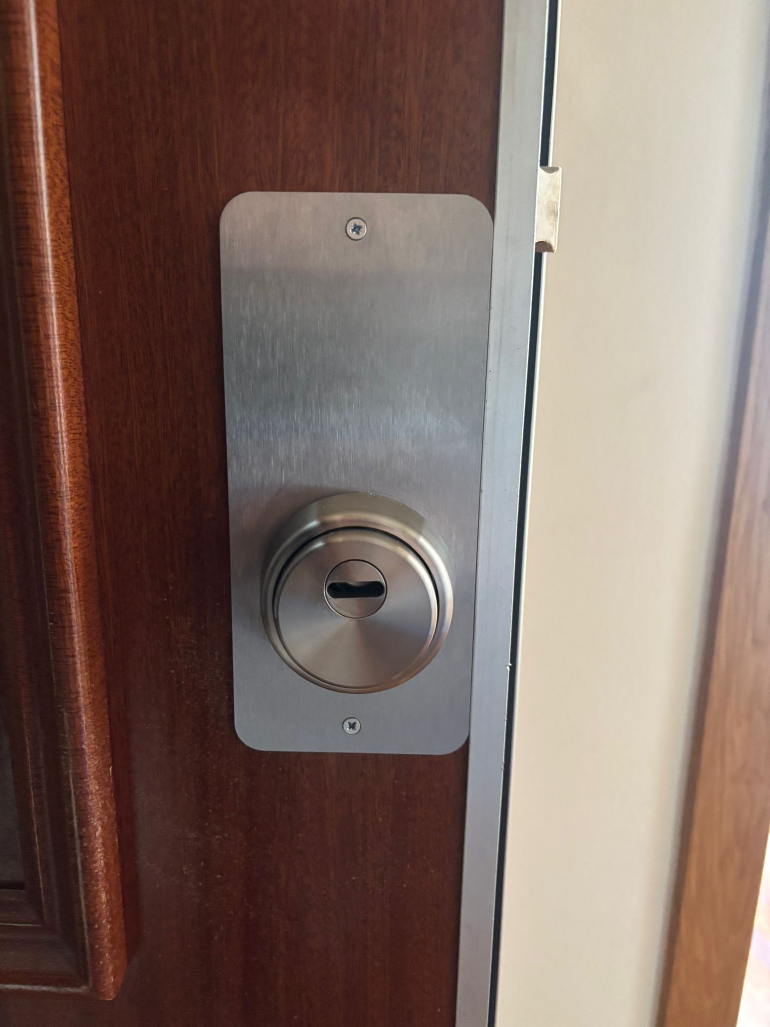 Escudo de seguridad rectangular en acero inoxidable satinado con bombín antipull instalado en puerta blindada de madera oscura